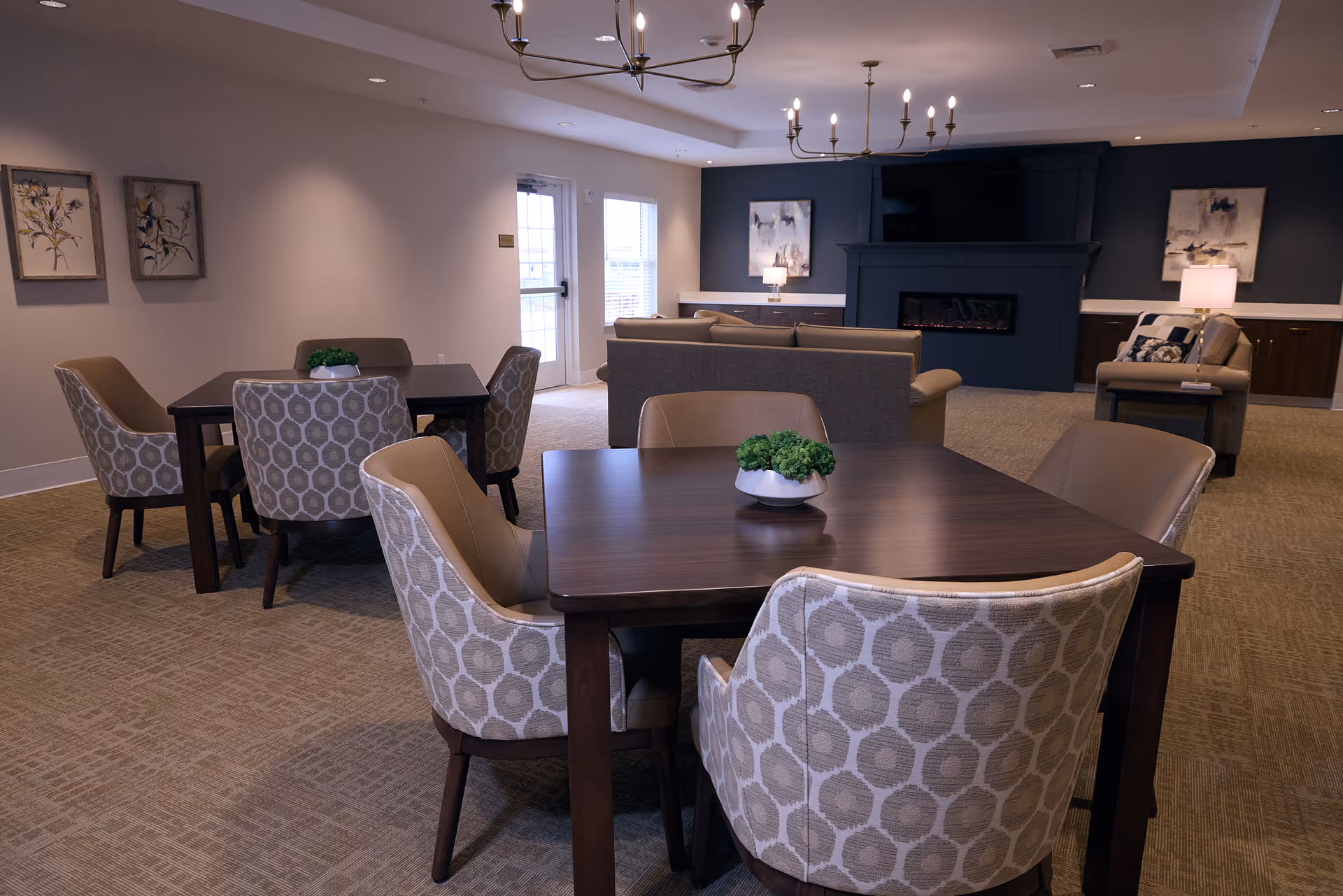 Interior common area with dark wood tables, cushioned patterned chairs, and a fireplace.