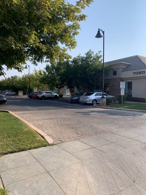 Exterior view of a senior facility with parked cars, trees, and a streetlamp.