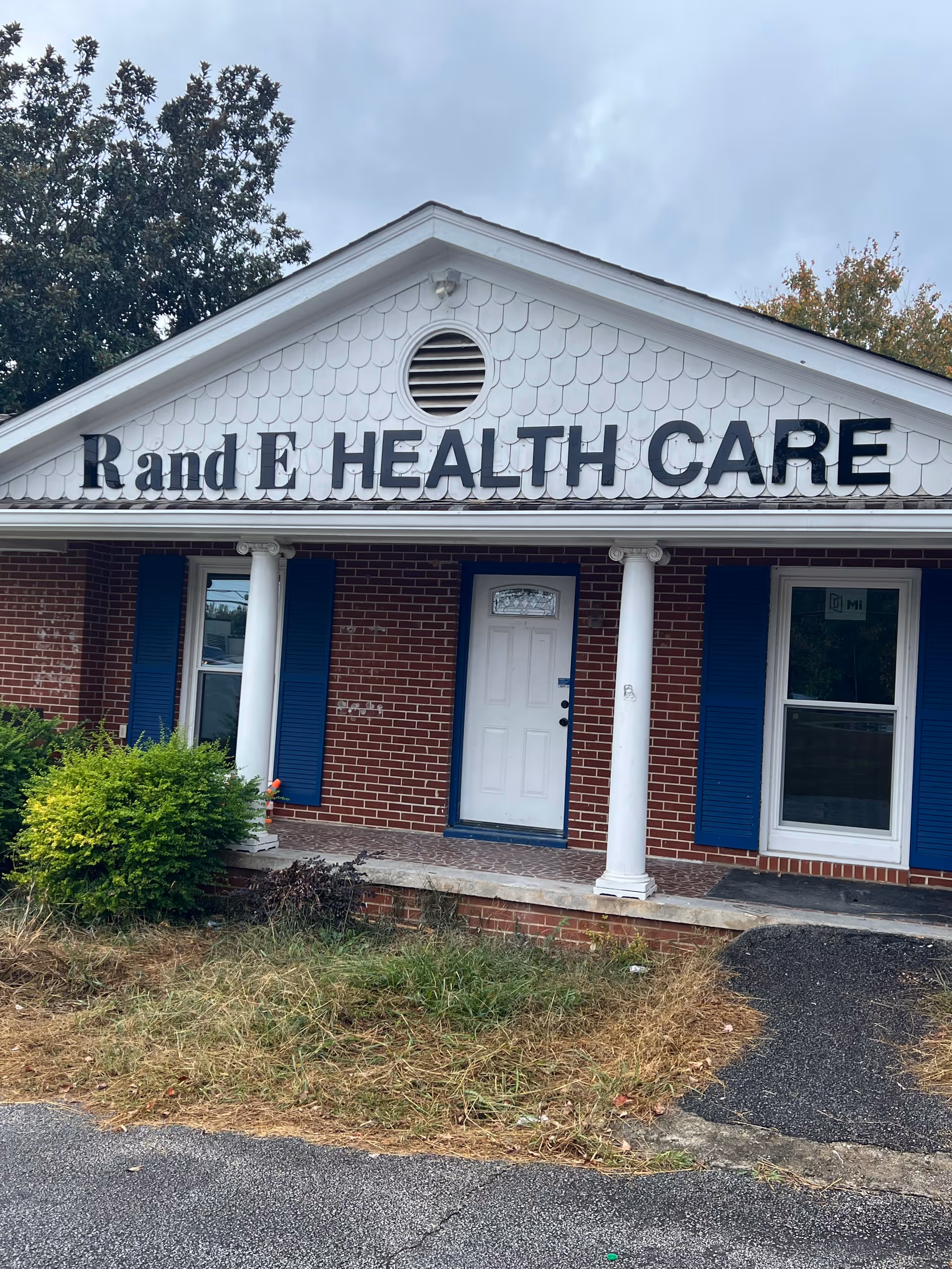 Front view of a brick building with white gable and sign 'R and E HEALTH CARE'.