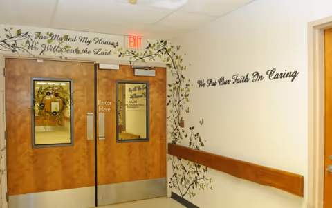 Double wooden doors with exit sign, floral wall mural, and hallway handrail.