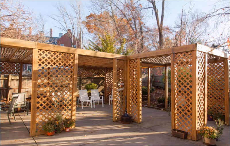 Outdoor patio area with wooden lattice pergolas, chairs, and potted plants.