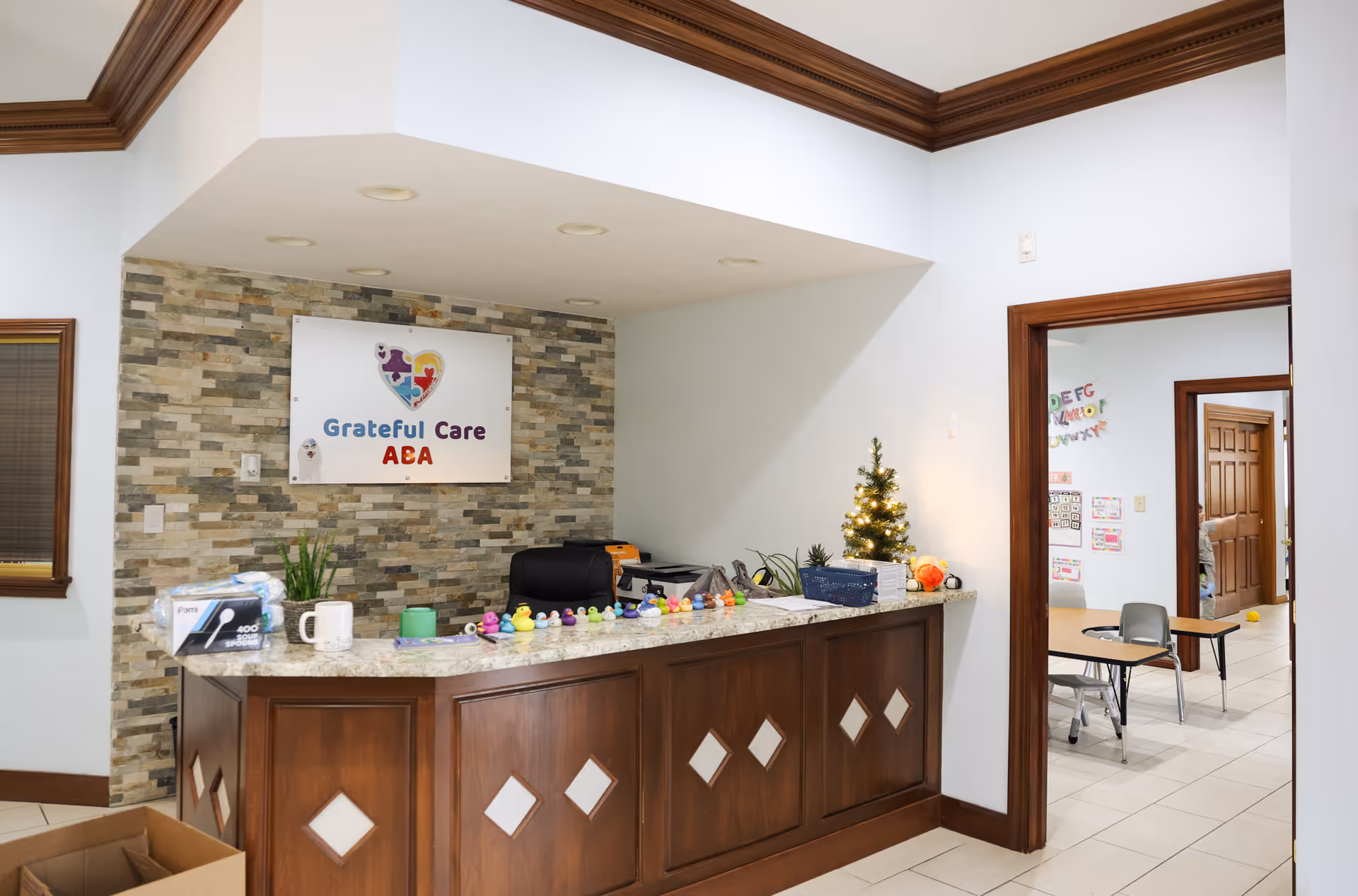 Wooden reception desk with stone backdrop, small Christmas tree, and doorway to offices.