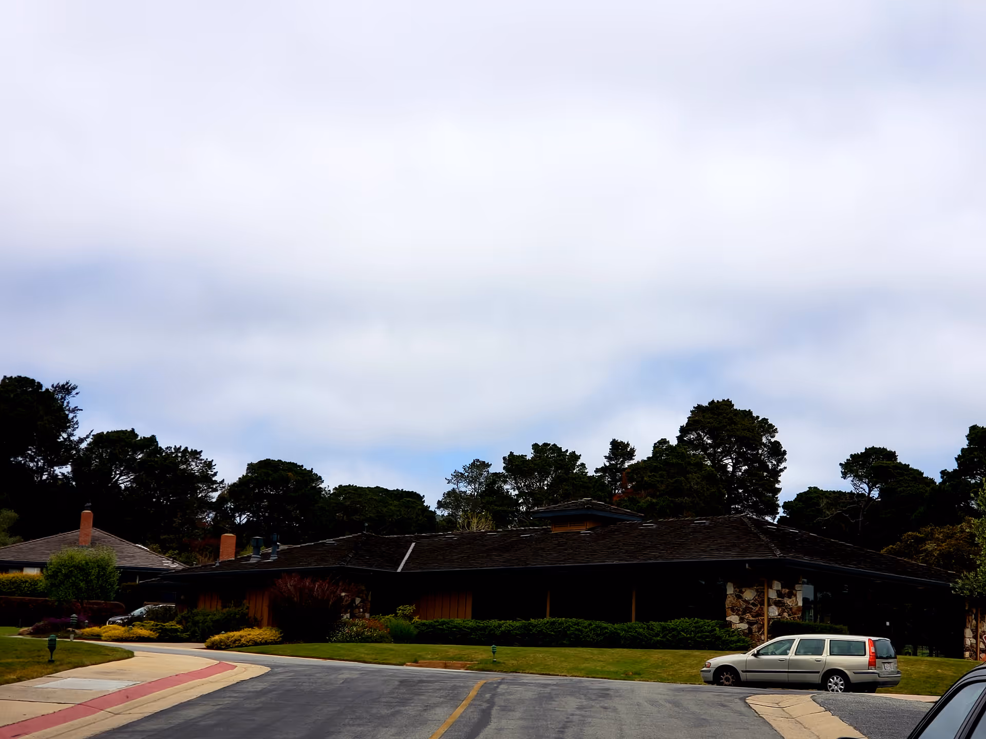 Exterior view of Del Mesa Carmel senior living campus with a low building and parked car.
