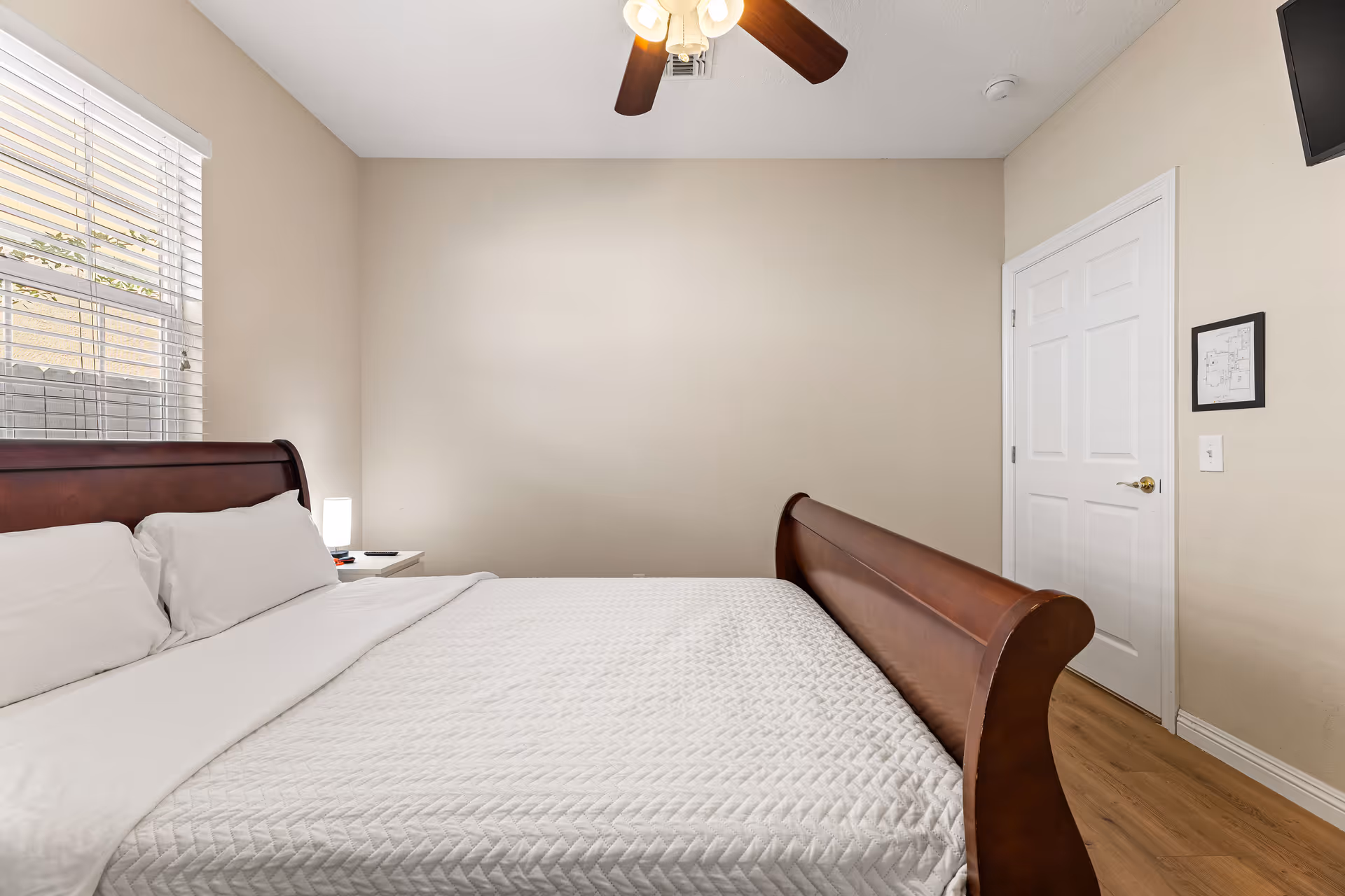 Tidy bedroom in a senior living facility with a large wooden bed and window.