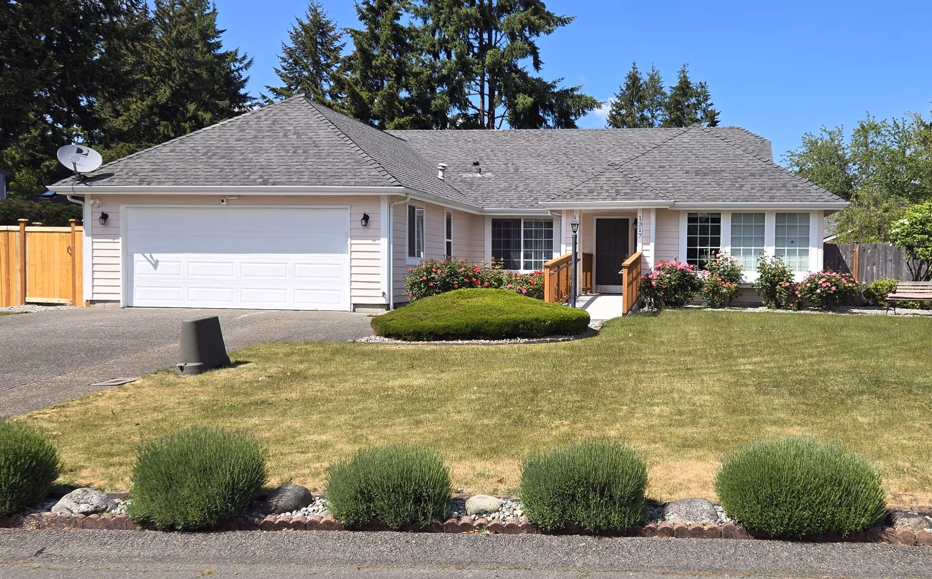 Single-story house with a two-car garage, manicured lawn, and flowering shrubs along the front.