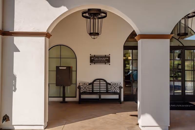 Exterior view of The Hacienda Mission San Luis Rey entrance with arches and bench.