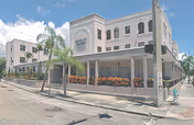 Three-story light-colored building labeled "Midtown Manor" with a covered ground-floor porch, palm trees, and a street in front.