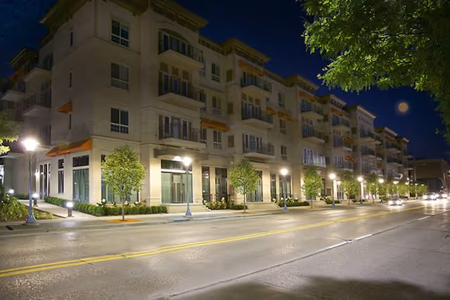 Nighttime exterior view of a multi-story senior living building with trees beside the street.