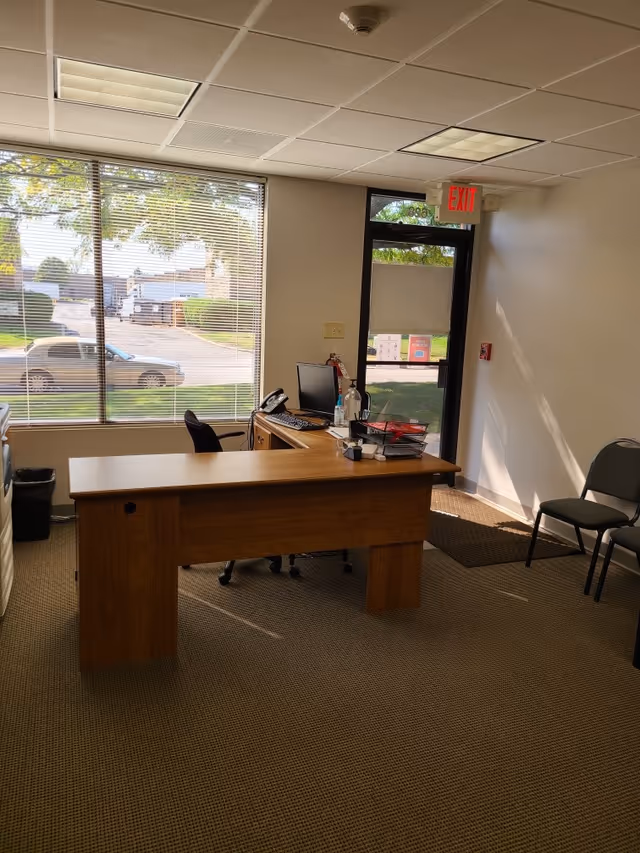 Wooden desk with computer and chairs inside a senior care facility office near a glass door.