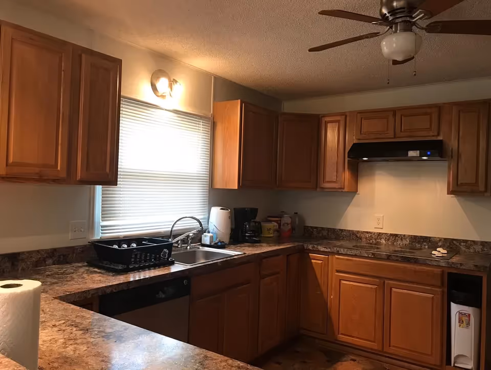 A kitchen with wooden cabinets, a sink and countertop appliances under a ceiling fan.