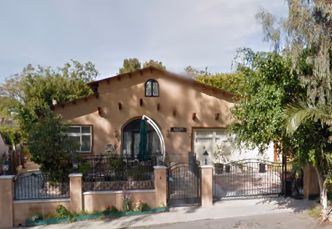 Front exterior of a single-story stucco senior living facility with arched doorway and iron gate.