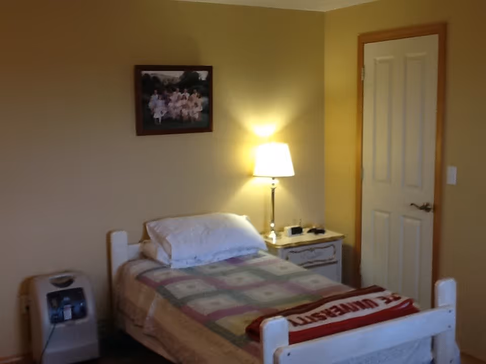 A small bedroom with bed, nightstand, lamp, framed photo, and door.