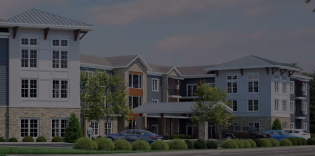 Modern multi-story senior living facility exterior with a covered entrance and parked cars.
