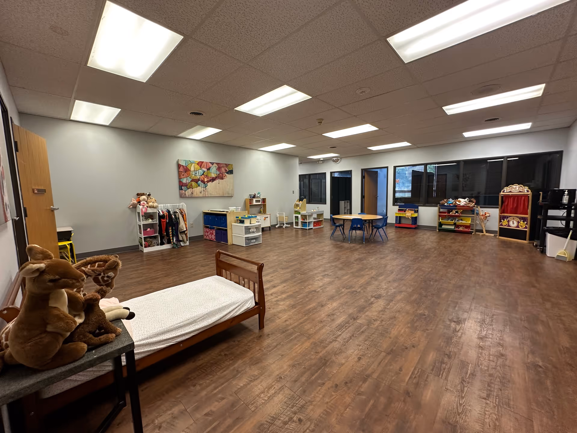A large, well-lit therapy/playroom with toys, shelves, and a bed along the left wall.