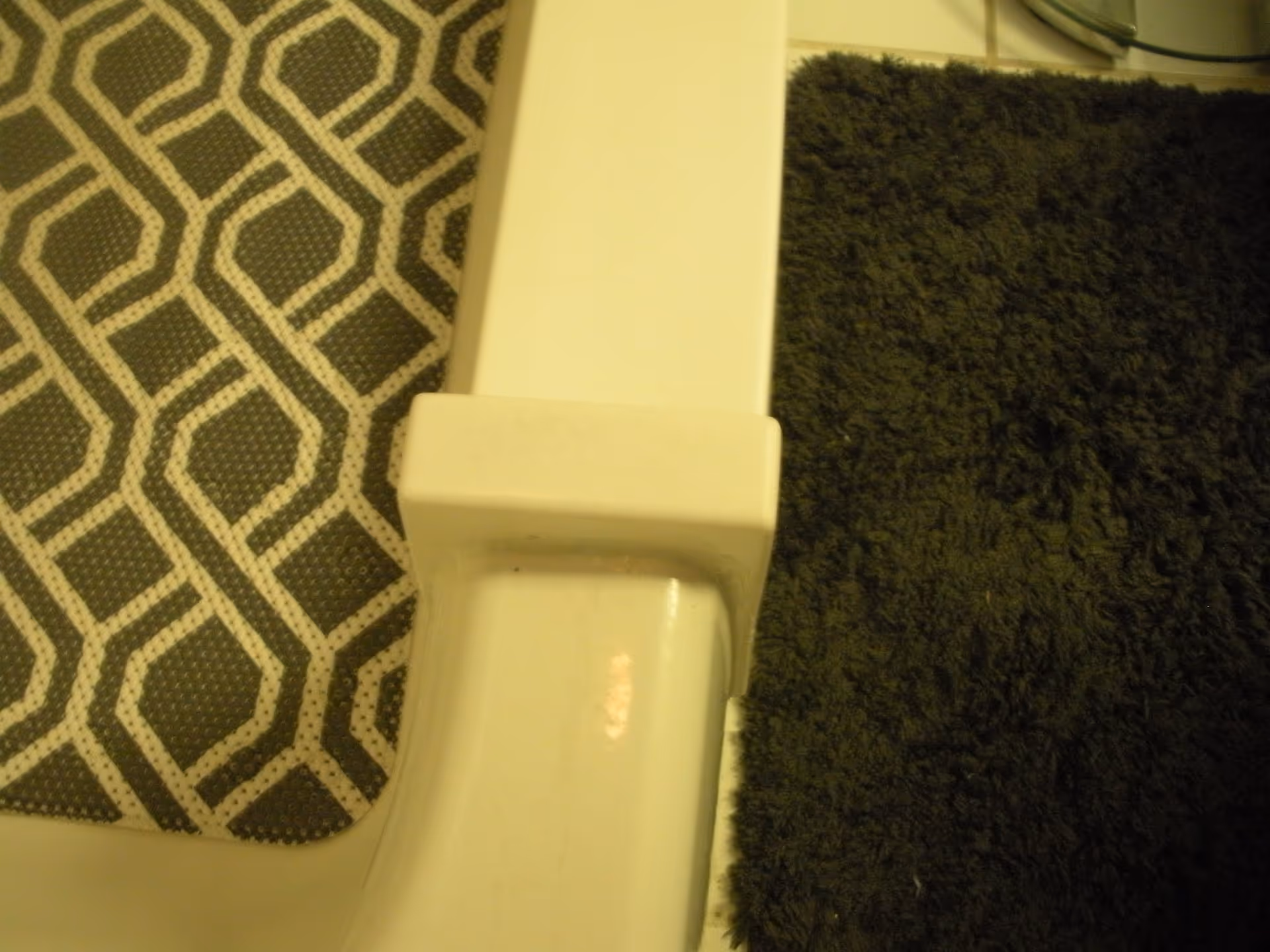 Close-up of a white toilet edge beside a black shag rug and geometric mat