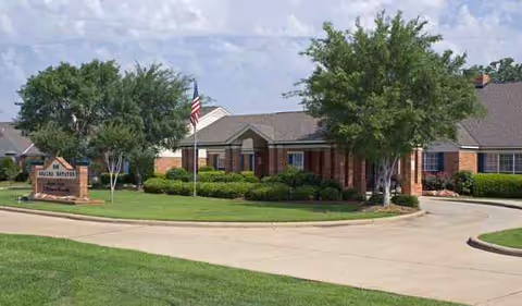 Exterior view of Azalea Estates of New Iberia with circular drive, flag, and landscaping.