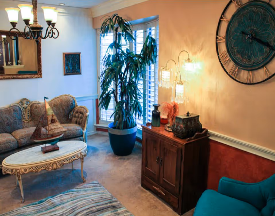 Cozy Victorian-style living room with patterned sofa, coffee table, plants, and decorative cabinet.