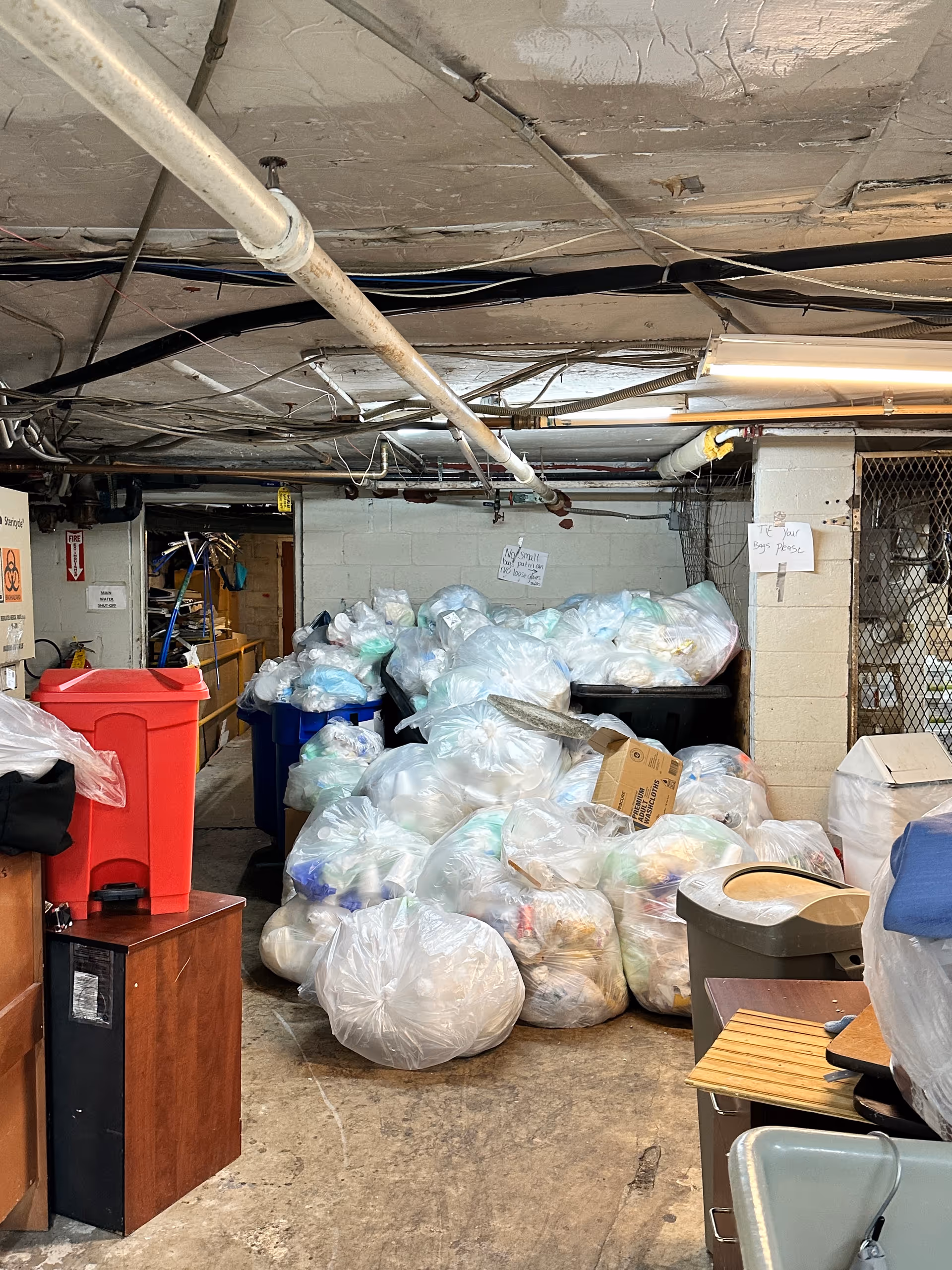 Basement storage area at Westbury Conyers with overflowing trash bags and exposed pipes.