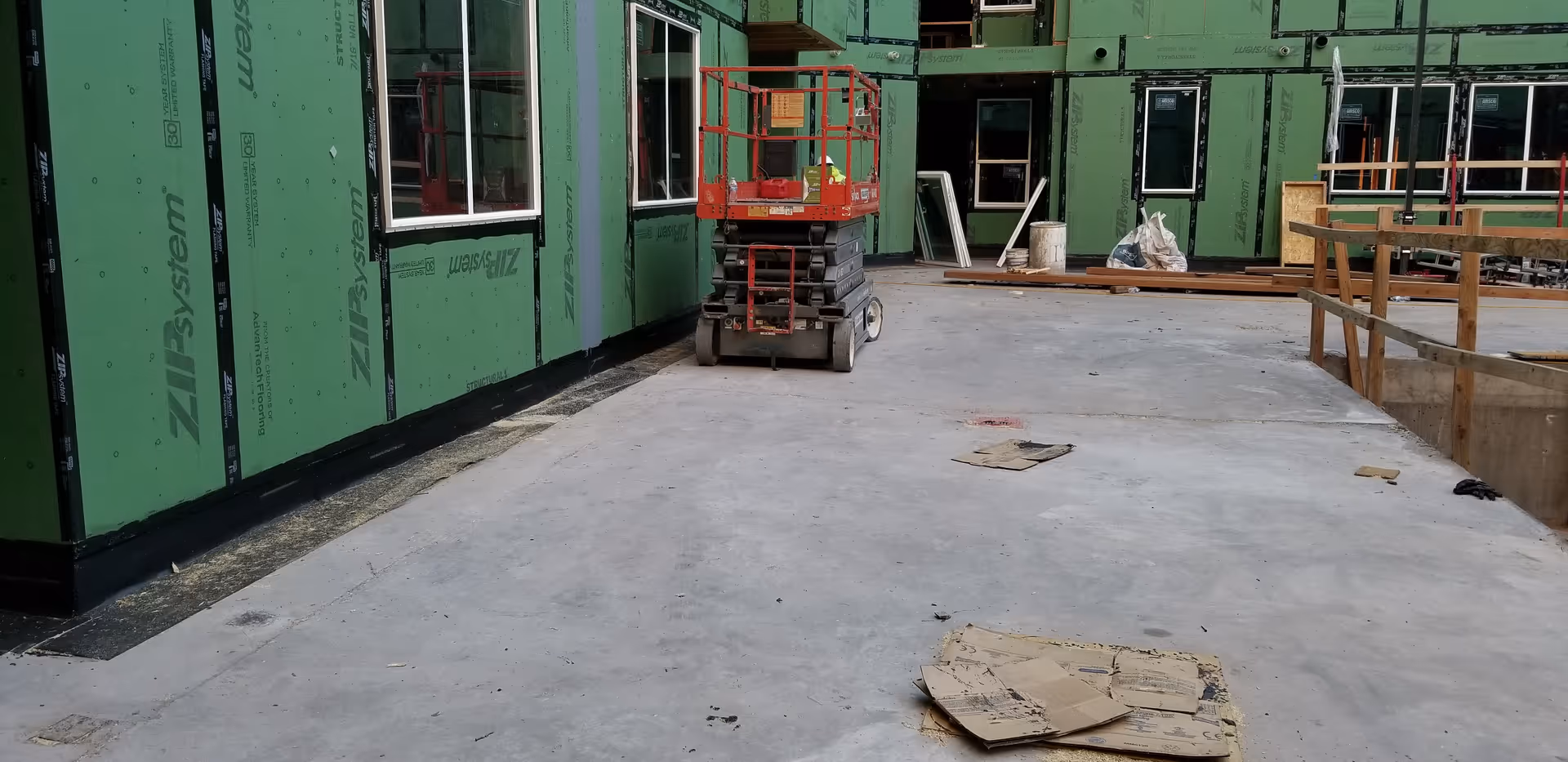 Exterior construction site with green sheathing, scaffolding, and a scissor lift.