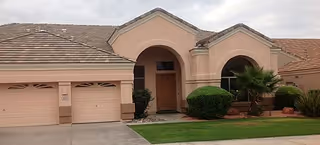 A single-story tan building with arched entry and two garage doors
