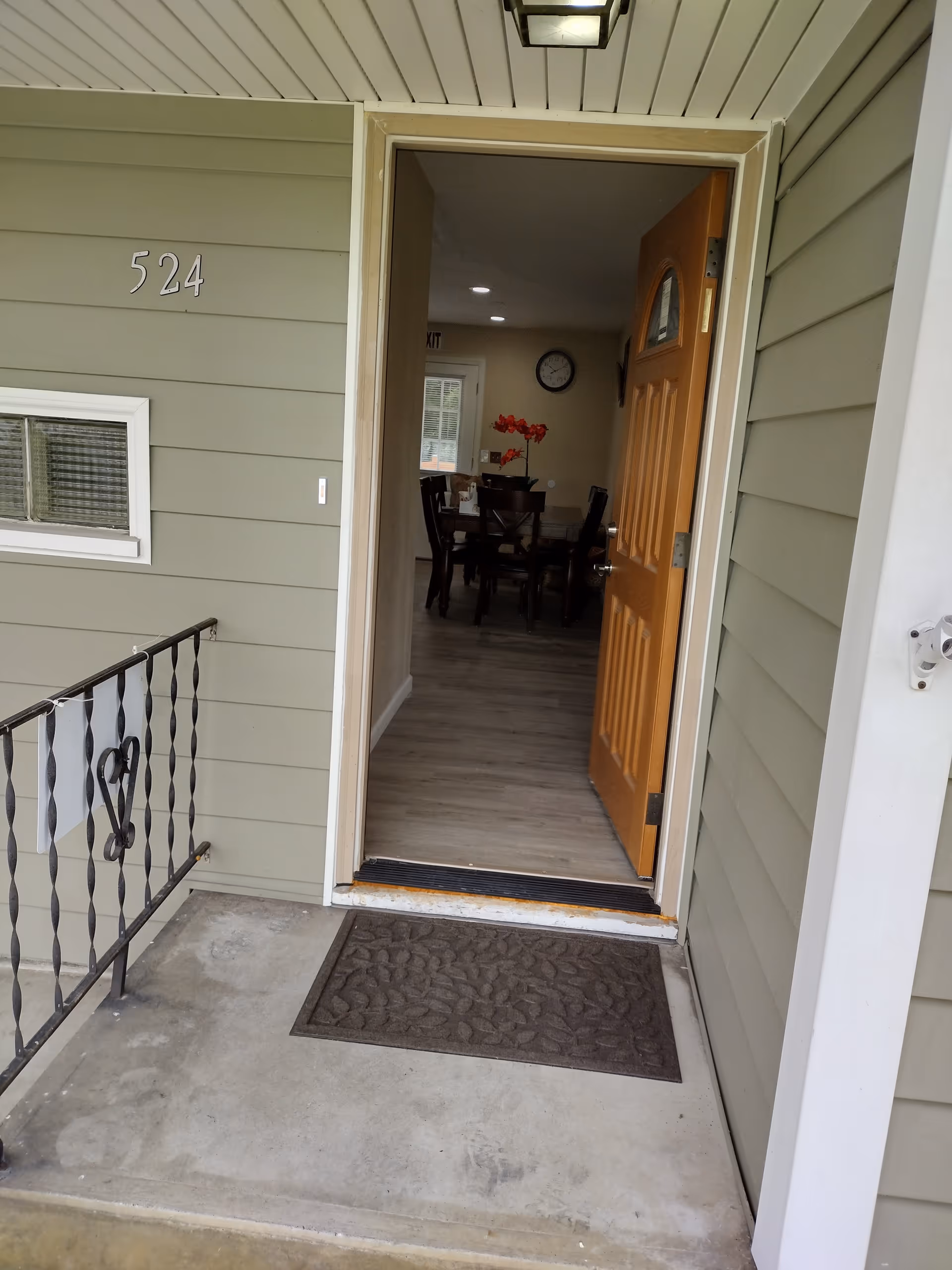 Open front door reveals a dining room with a table and red flowers.