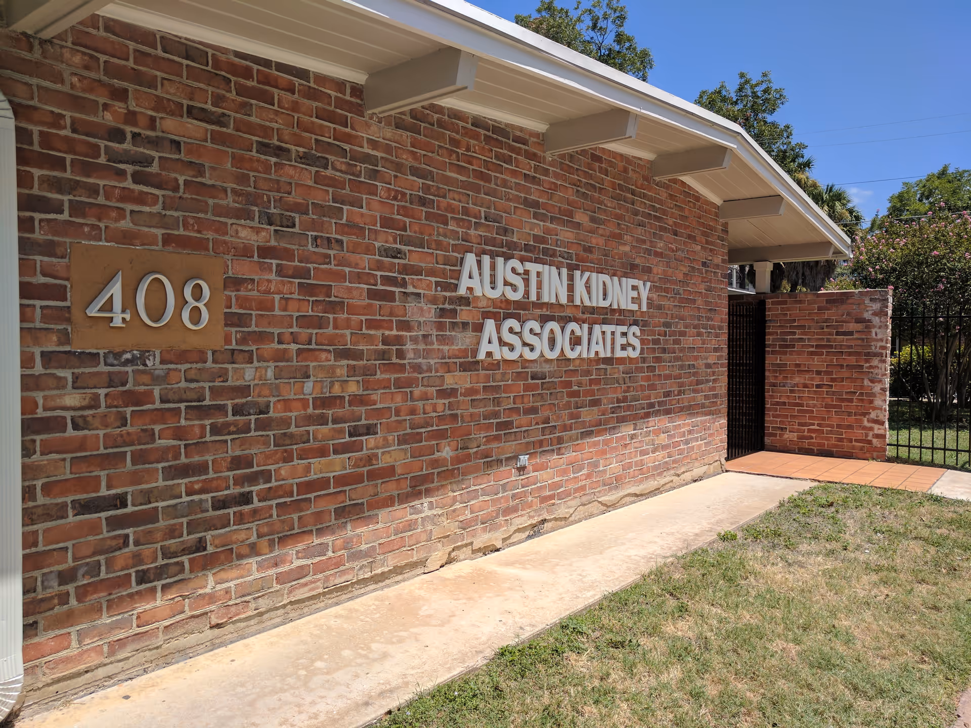 Brick exterior wall with Austin Kidney Associates sign and address 408 in daylight.