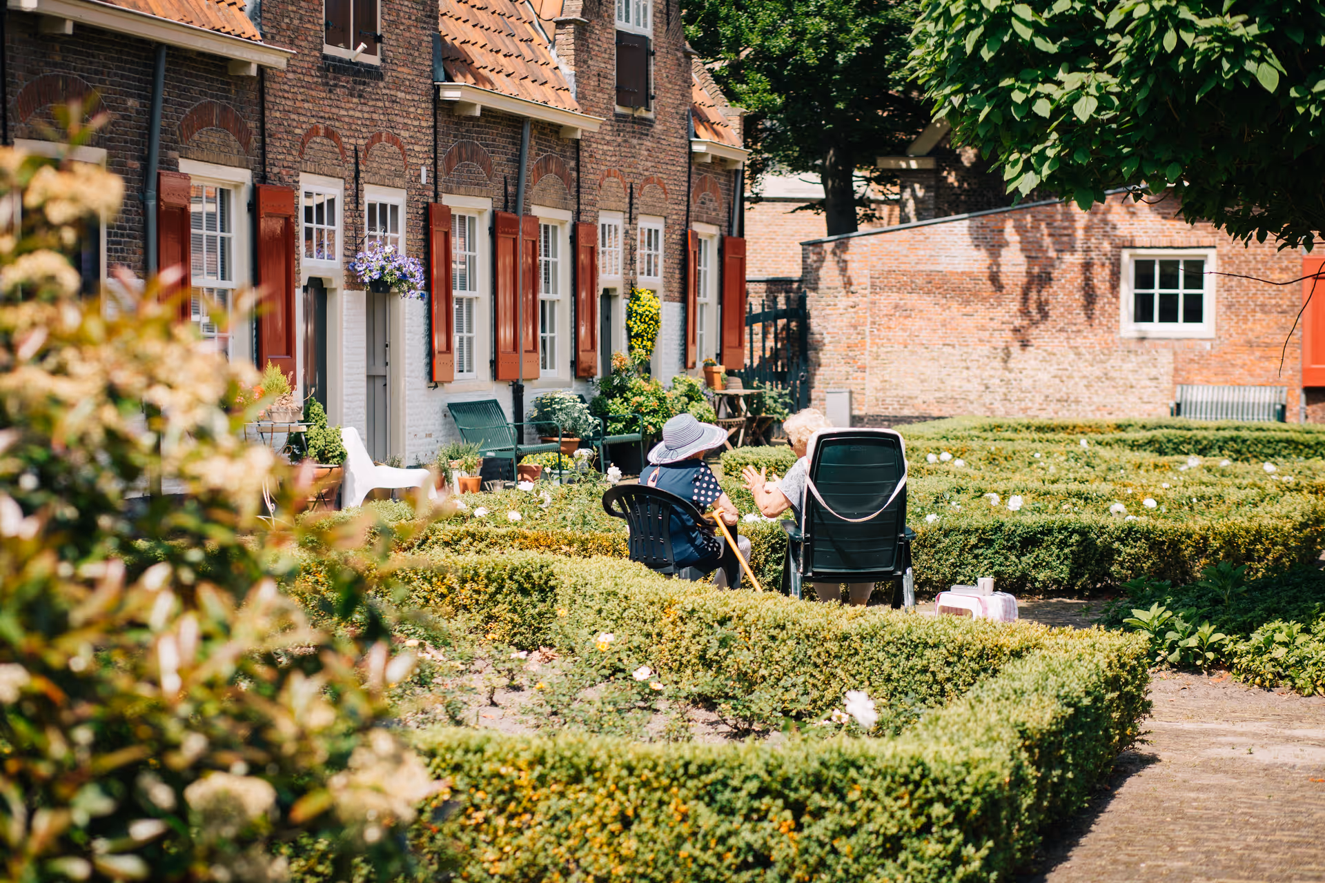Outdoor courtyard of Mercy Home Health Services with hedges, brick buildings, and residents sitting in chairs.