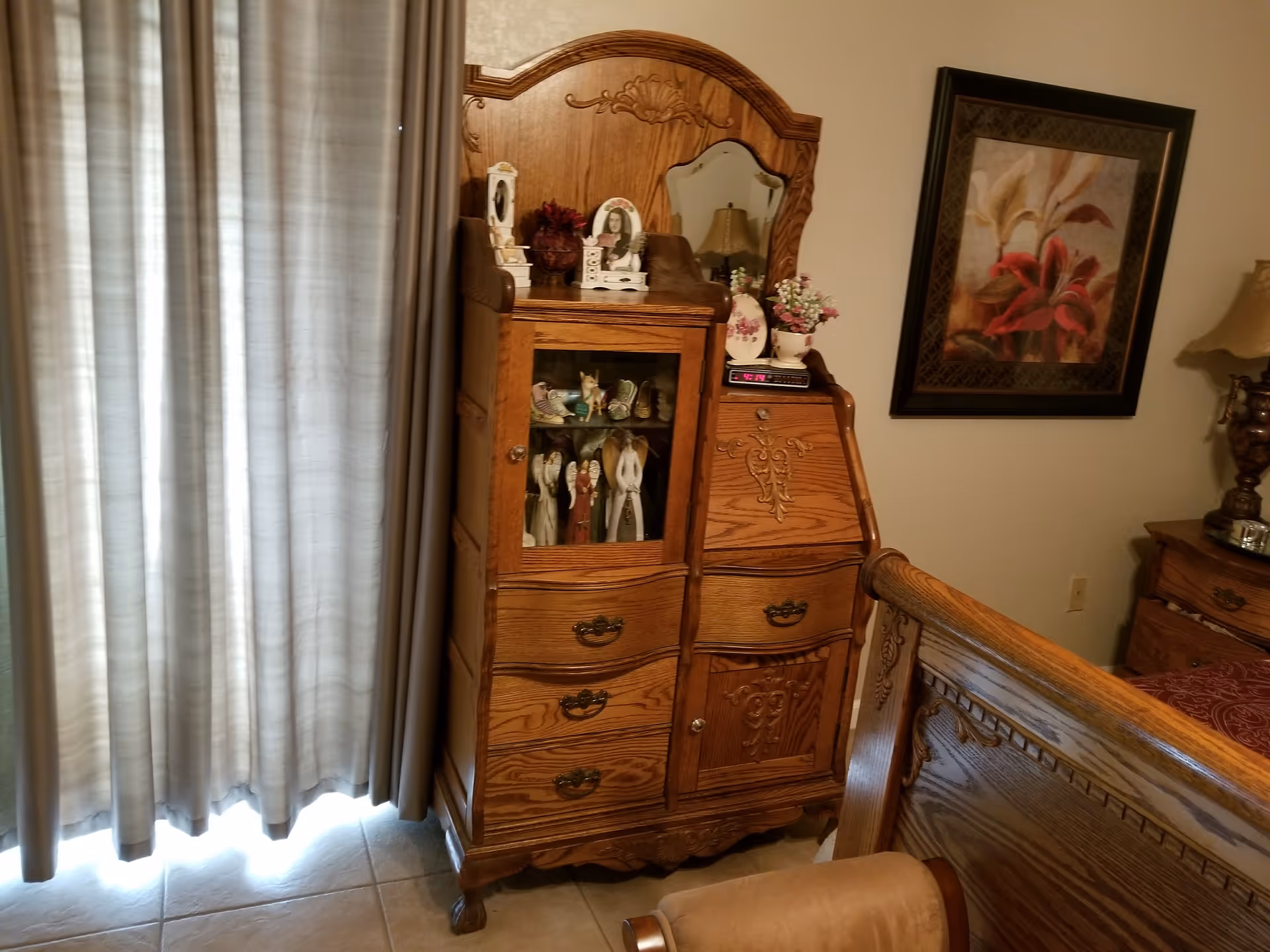 Oak dresser with mirror and floral decor beside a bed in a cozy bedroom.