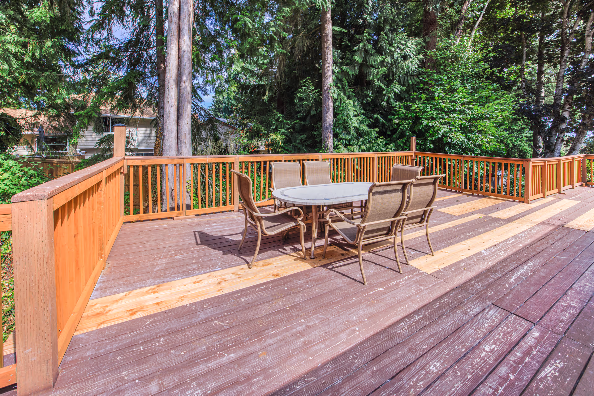 A wooden outdoor deck with a round table and chairs amid trees.
