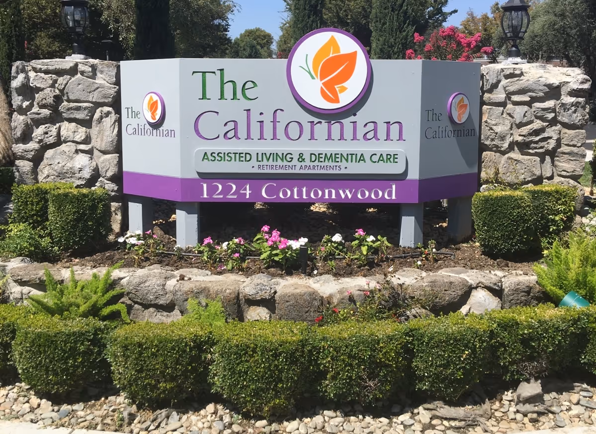 Colorful exterior sign for The Californian assisted living surrounded by landscaped shrubs.