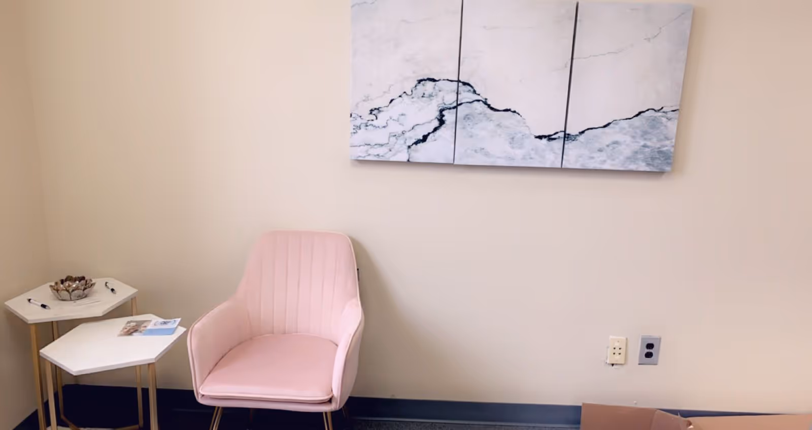 Pink upholstered chair beside small white tables in a neutral-toned lounge area.