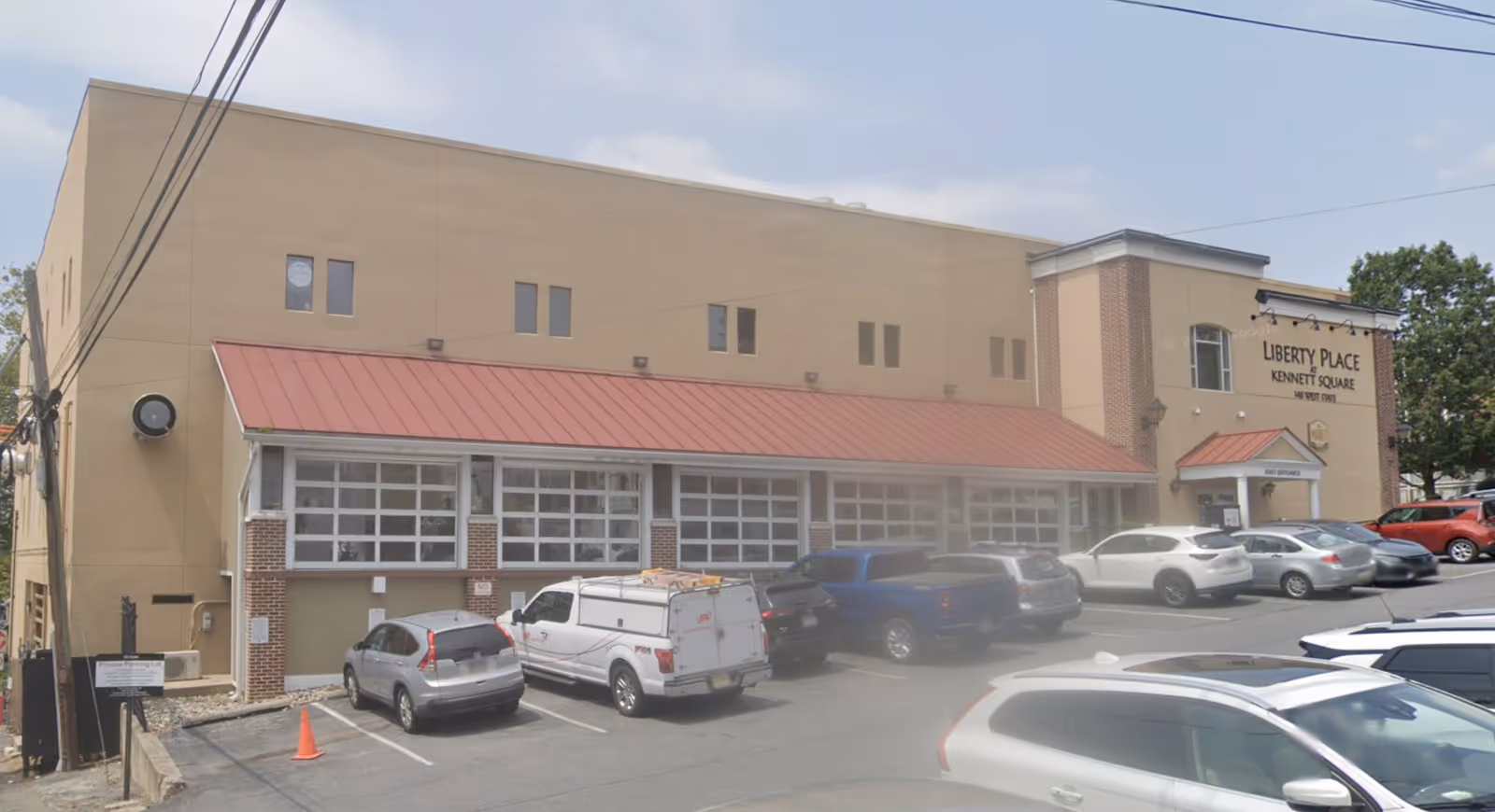 Exterior view of a beige building with a red awning, multiple windows, and parked cars.