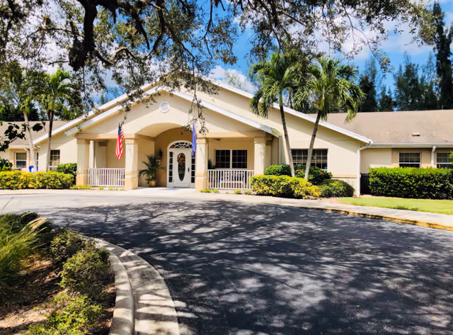 Arden Courts Fort Myers front entrance of a light beige senior living facility with flags.