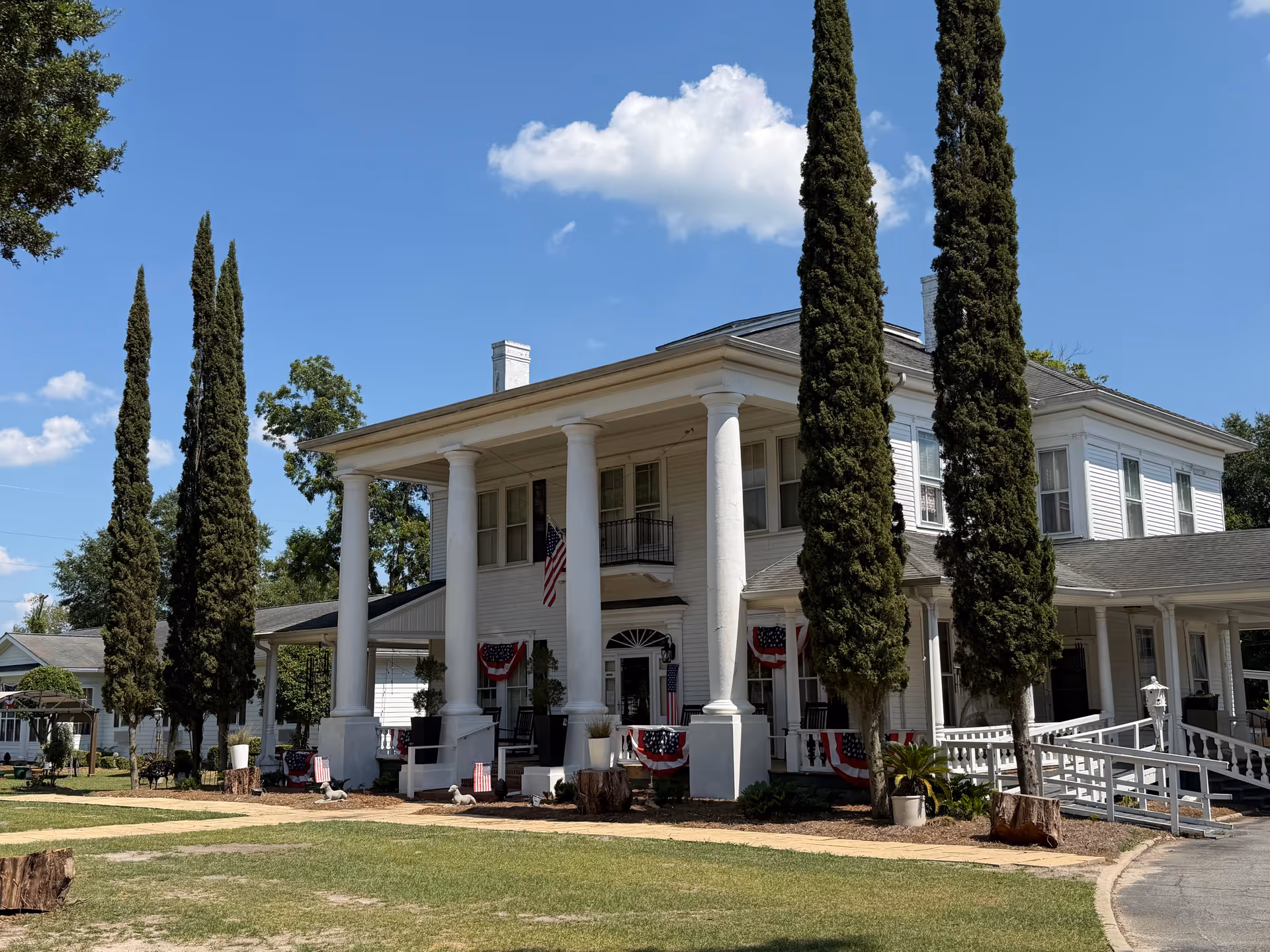 White two-story building with tall columns and patriotic bunting on a sunny day.