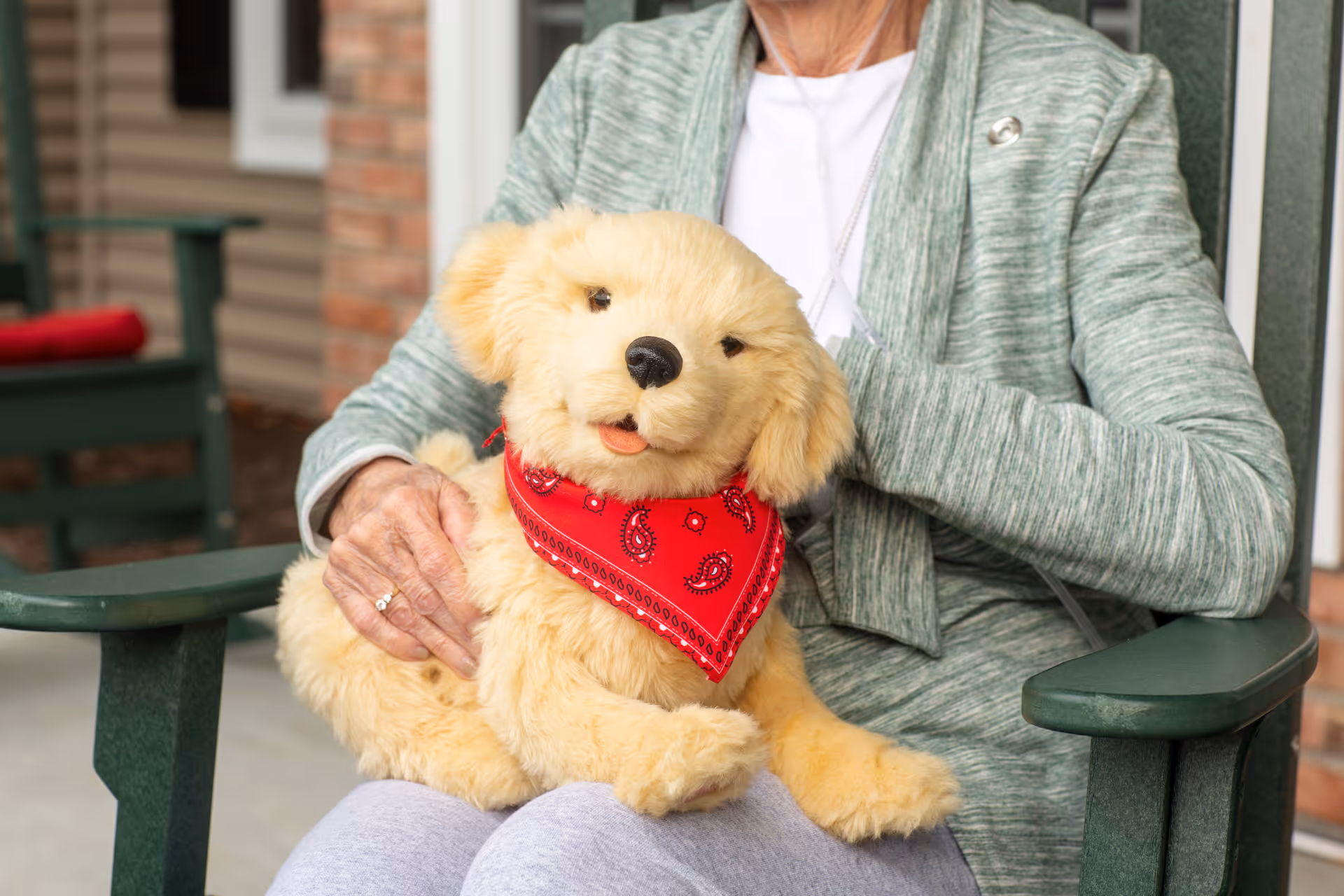 Senior resident sits on a porch holding a fluffy golden puppy with a red bandana.