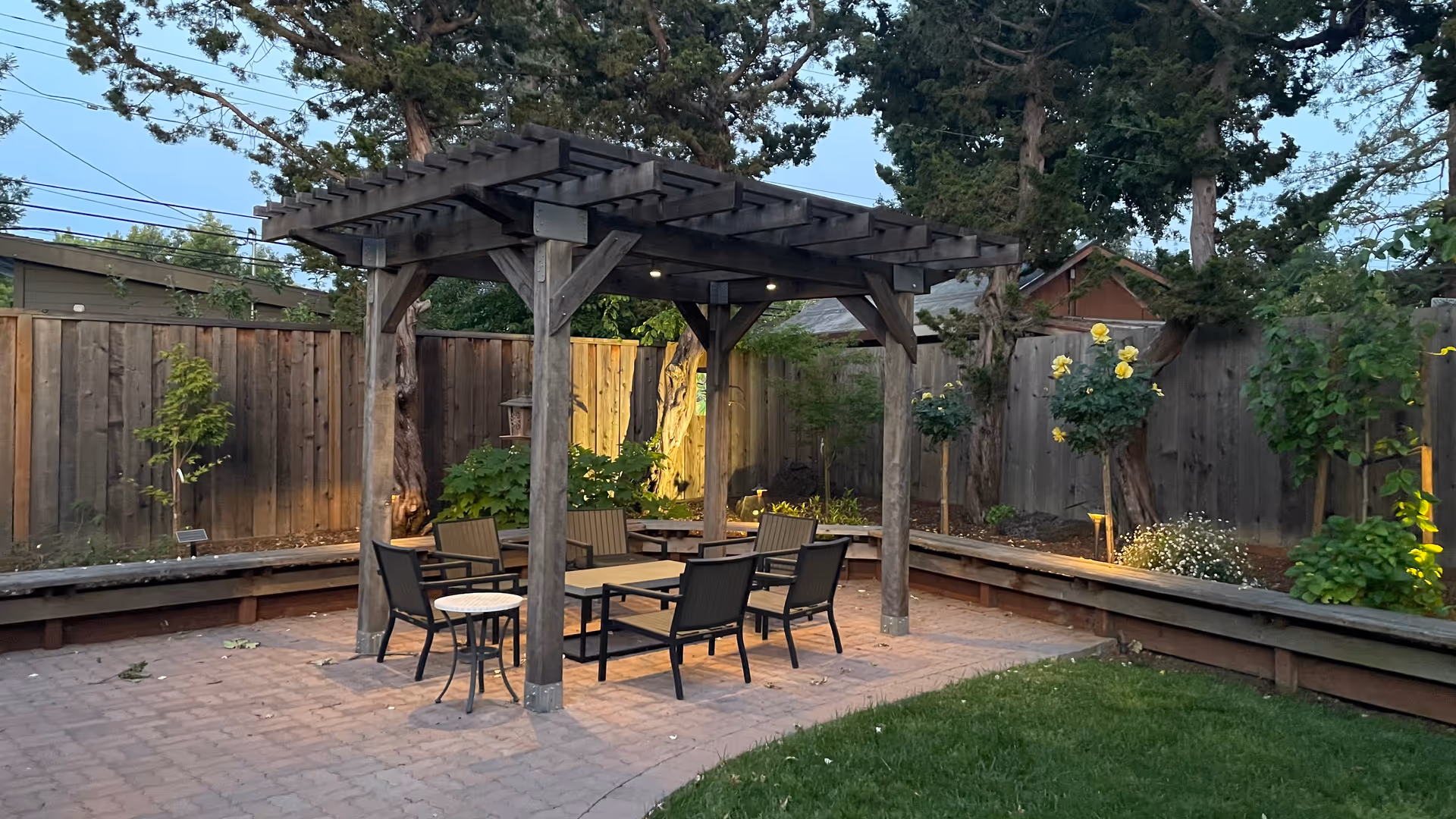 Outdoor brick patio under a wooden pergola with seating and garden beds.