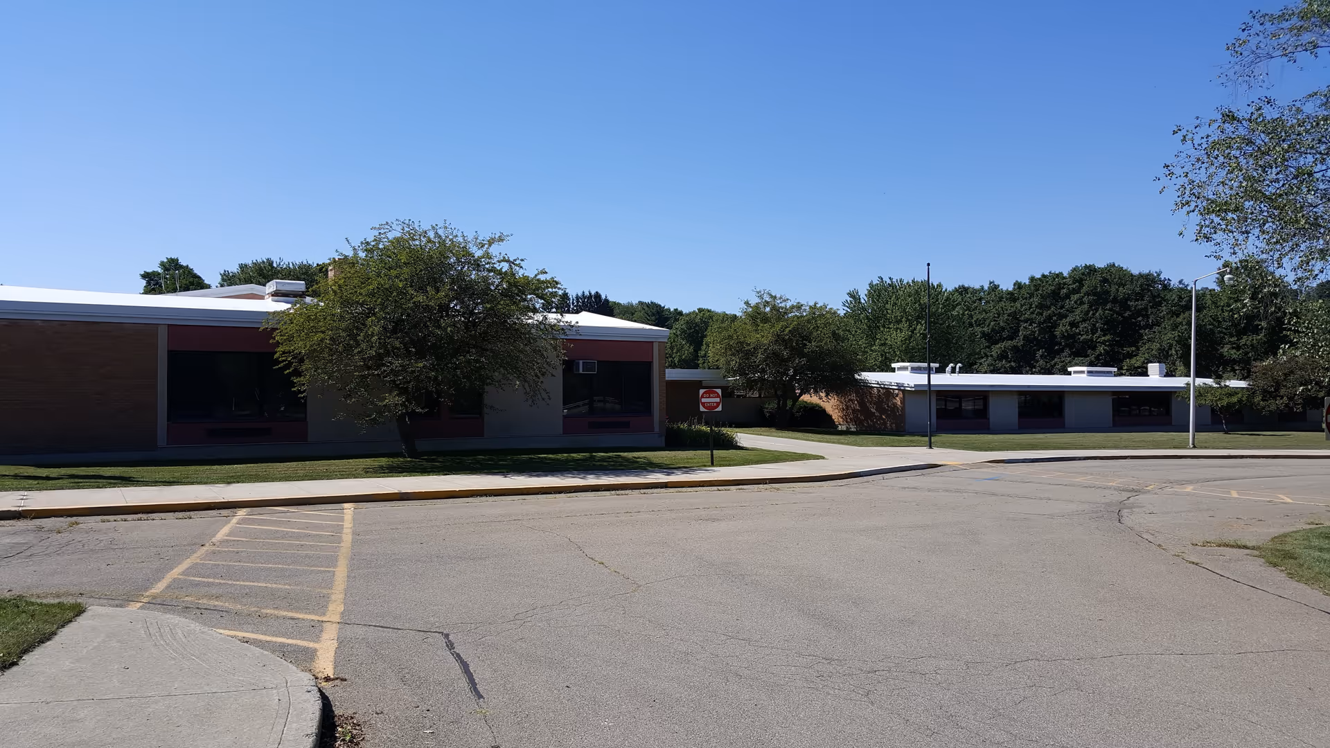 Single-story care facility exterior with parking lot, trees, and a clear blue sky.