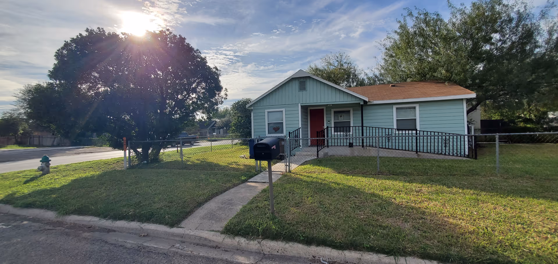 A small teal single-story facility with a ramp, mailbox, and green lawn on a residential street.