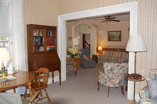 Traditional living room with sofas, lamps, a bookshelf, and a round dining table.