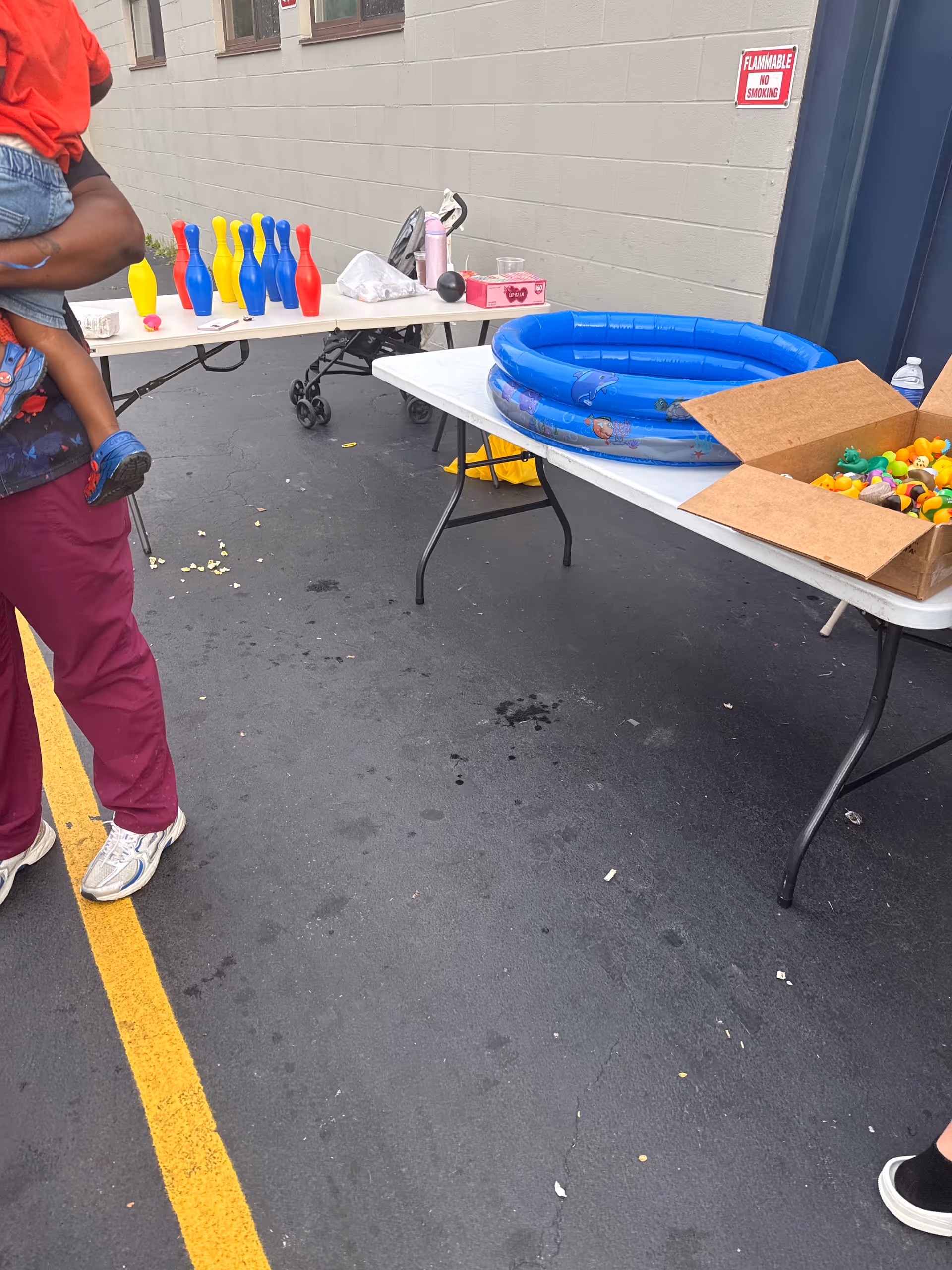 Outdoor activity area with tables, toys, a blue inflatable pool, and a person carrying a child.