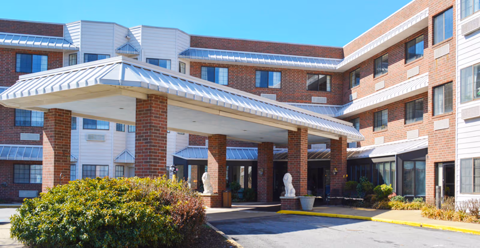Brick senior living facility with a covered porte-cochere entrance and landscaped shrubs.