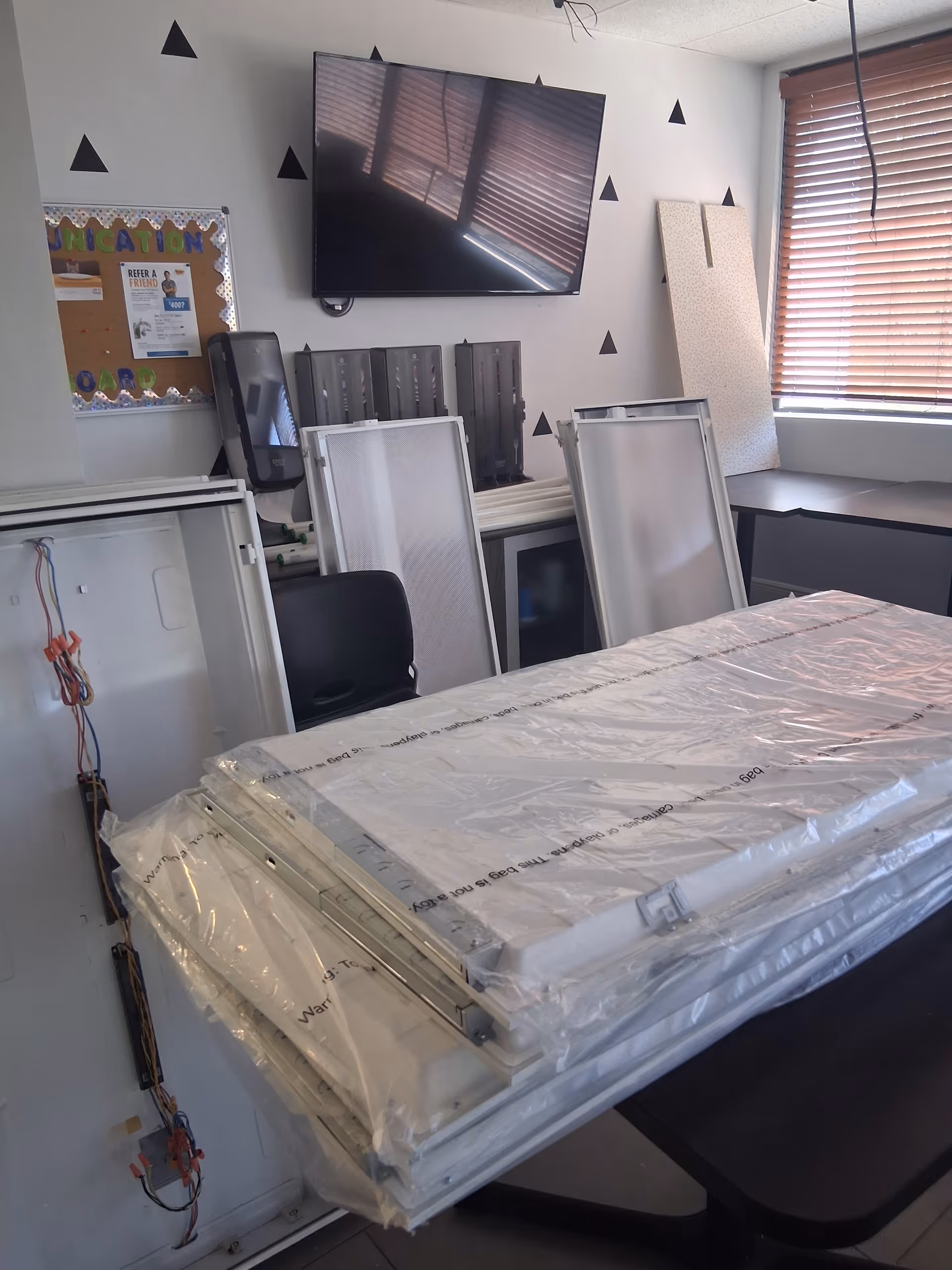 Interior room with a wrapped hospital bed, wall-mounted TV, and stacked equipment.