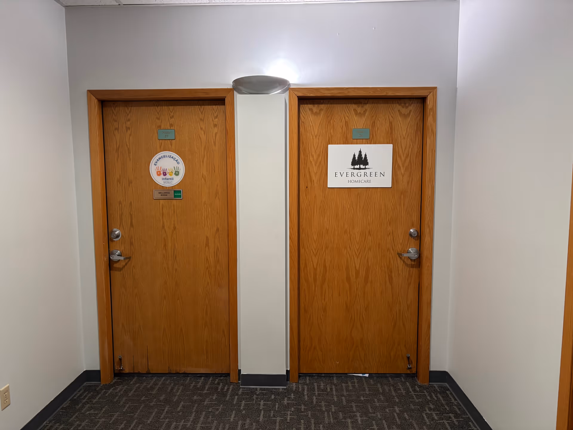 Two wooden doors in a hallway, one labeled Evergreen Homecare, with signs.