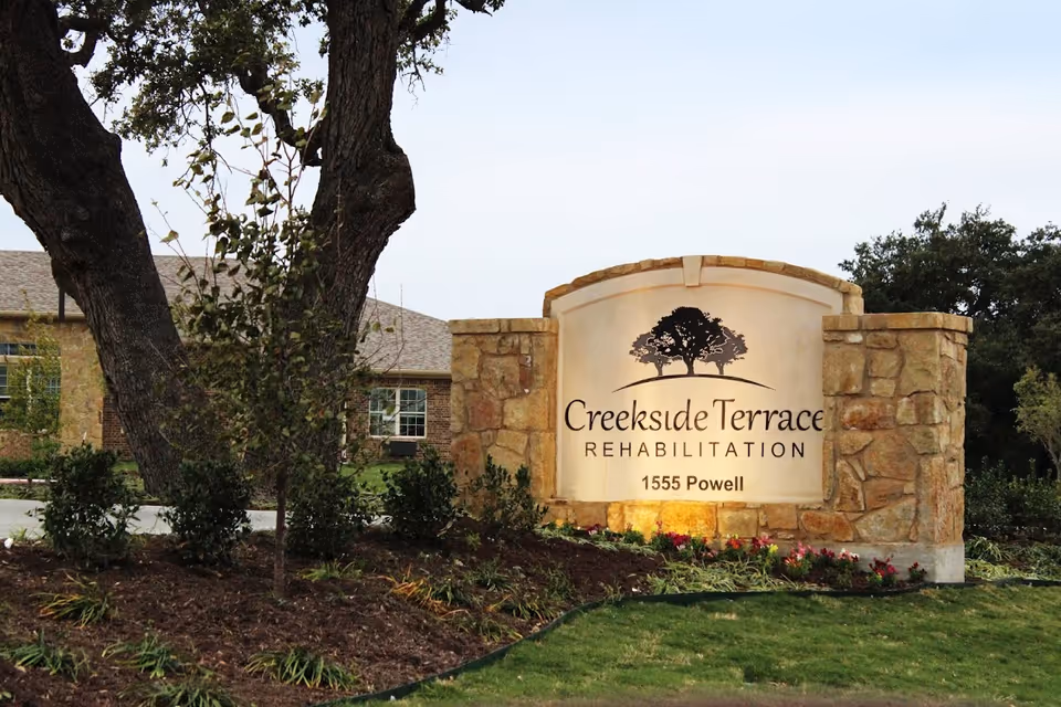Stone entrance sign reading Creekside Terrace Rehabilitation with trees and landscaping surrounding.