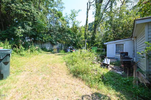 Overgrown backyard with a small house, scattered chairs, grills, and dense vegetation.