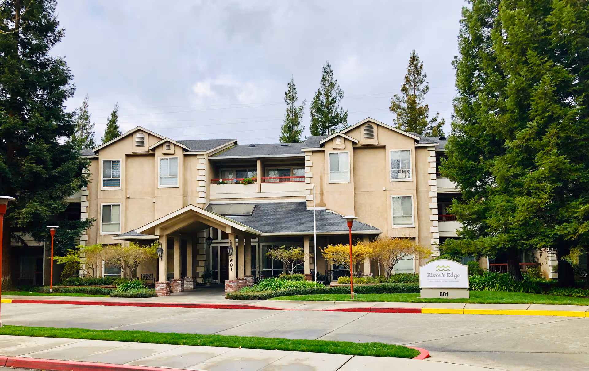 Front view of River's Edge senior living building with entrance, sign, and trees.