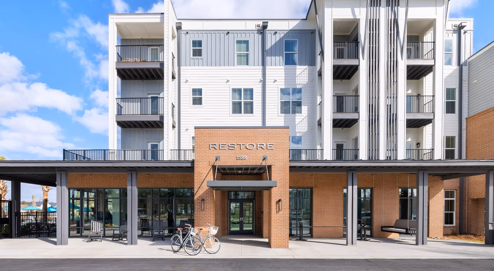Front exterior view of Restore at Carolina Park building with a brick entrance, large windows, balconies, and two bicycles parked outside under a covered walkway.