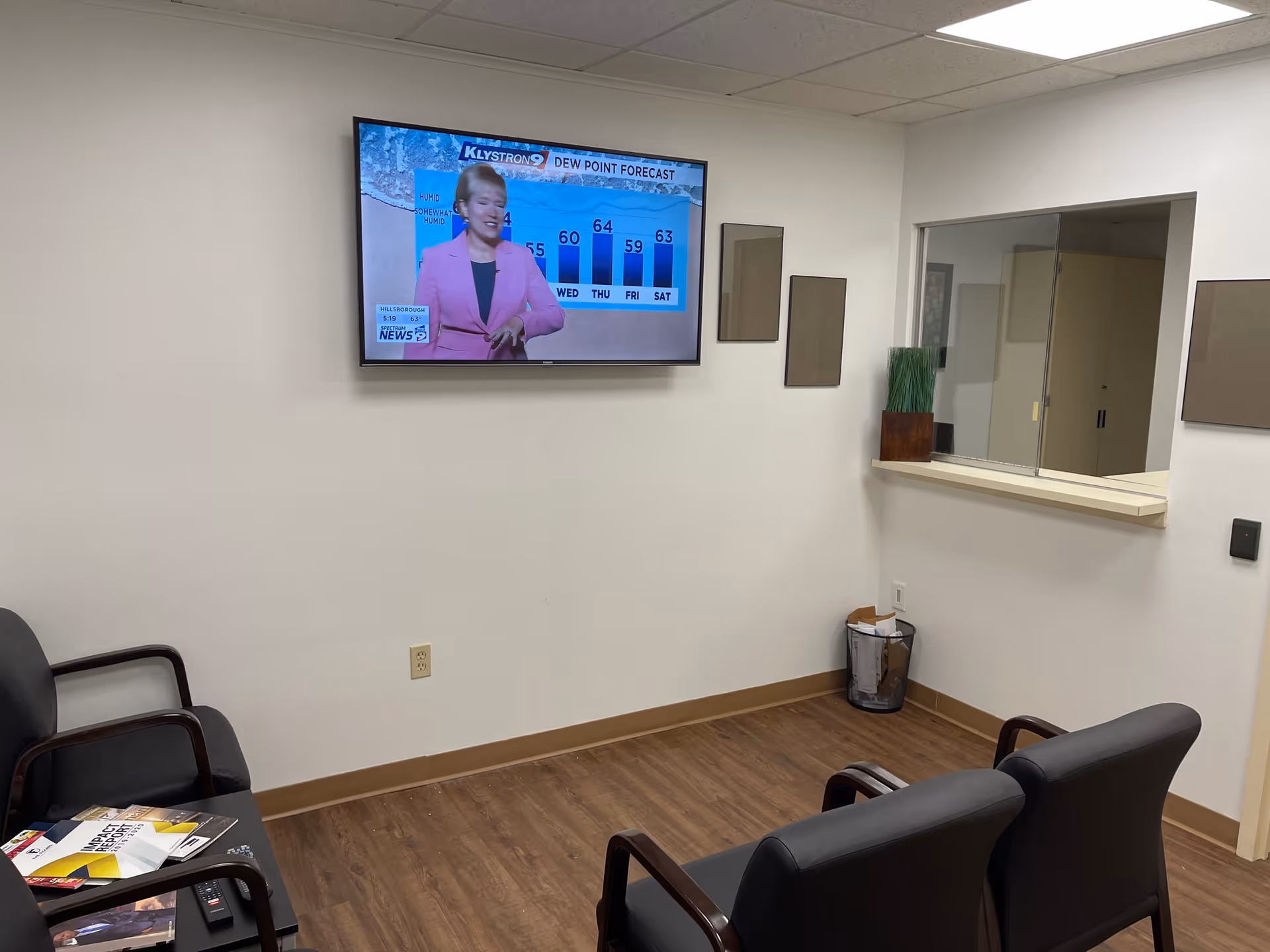 A small waiting area with black chairs and a wall-mounted TV showing a weather forecast.