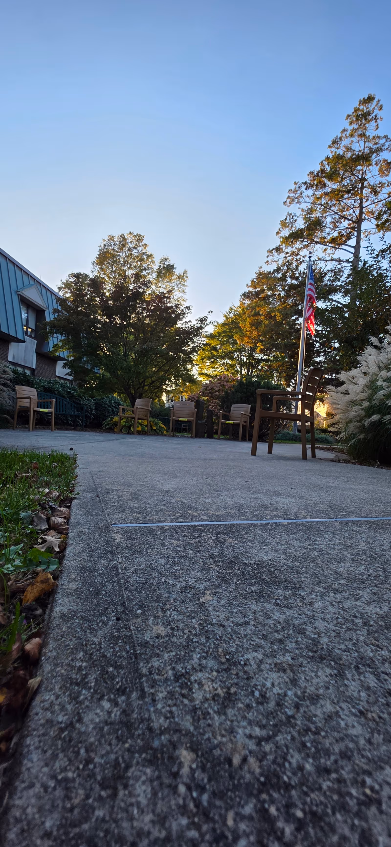 Outdoor patio at New Bedford Jewish Convalescent Home with chairs, flag, and trees.