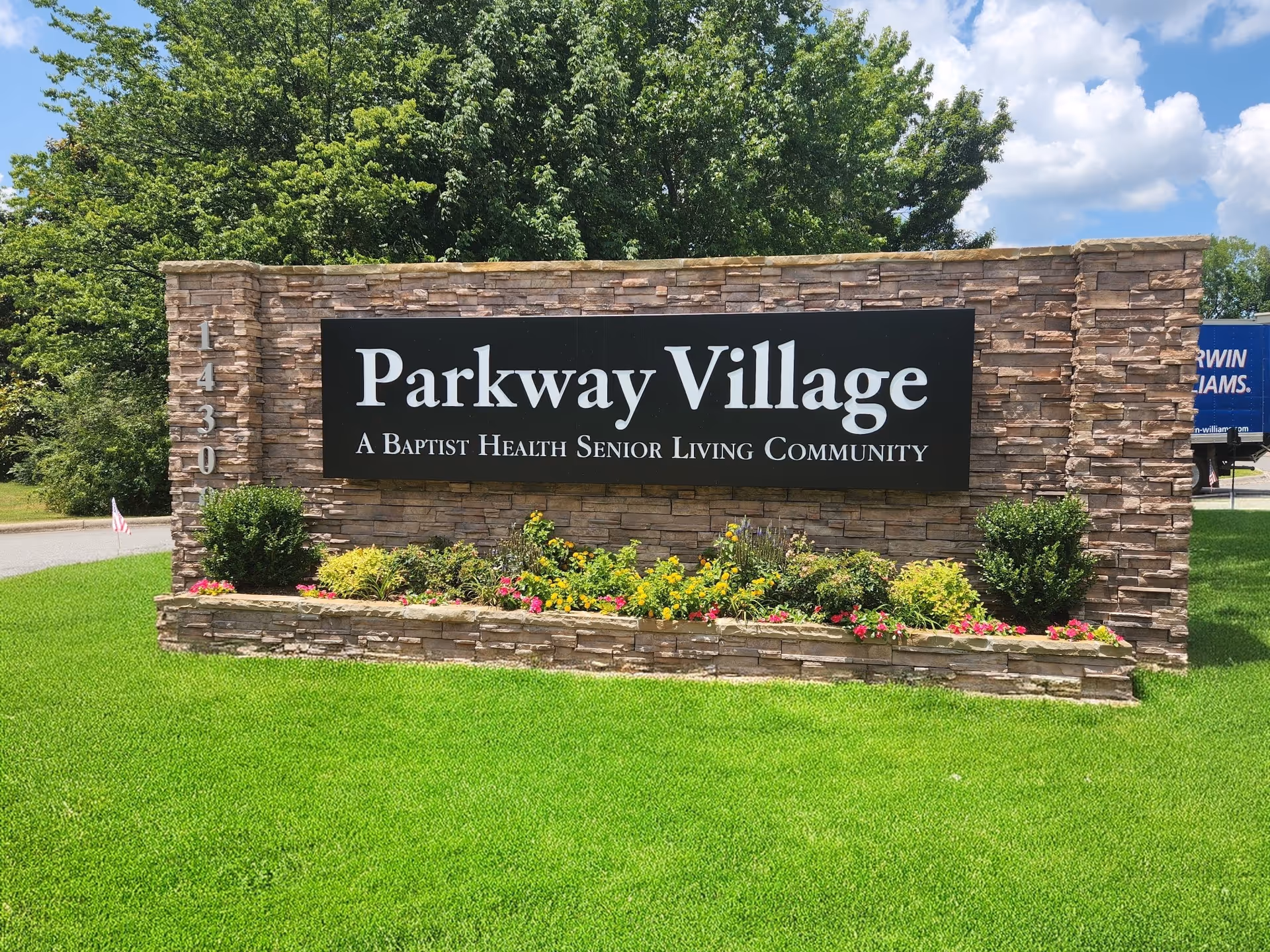 Stone sign reads Parkway Village Senior Living Community with a flower bed.